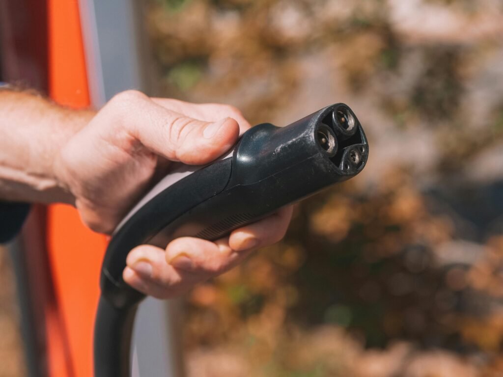 Hand holding an electric vehicle charging plug, symbolizing clean energy and innovation.